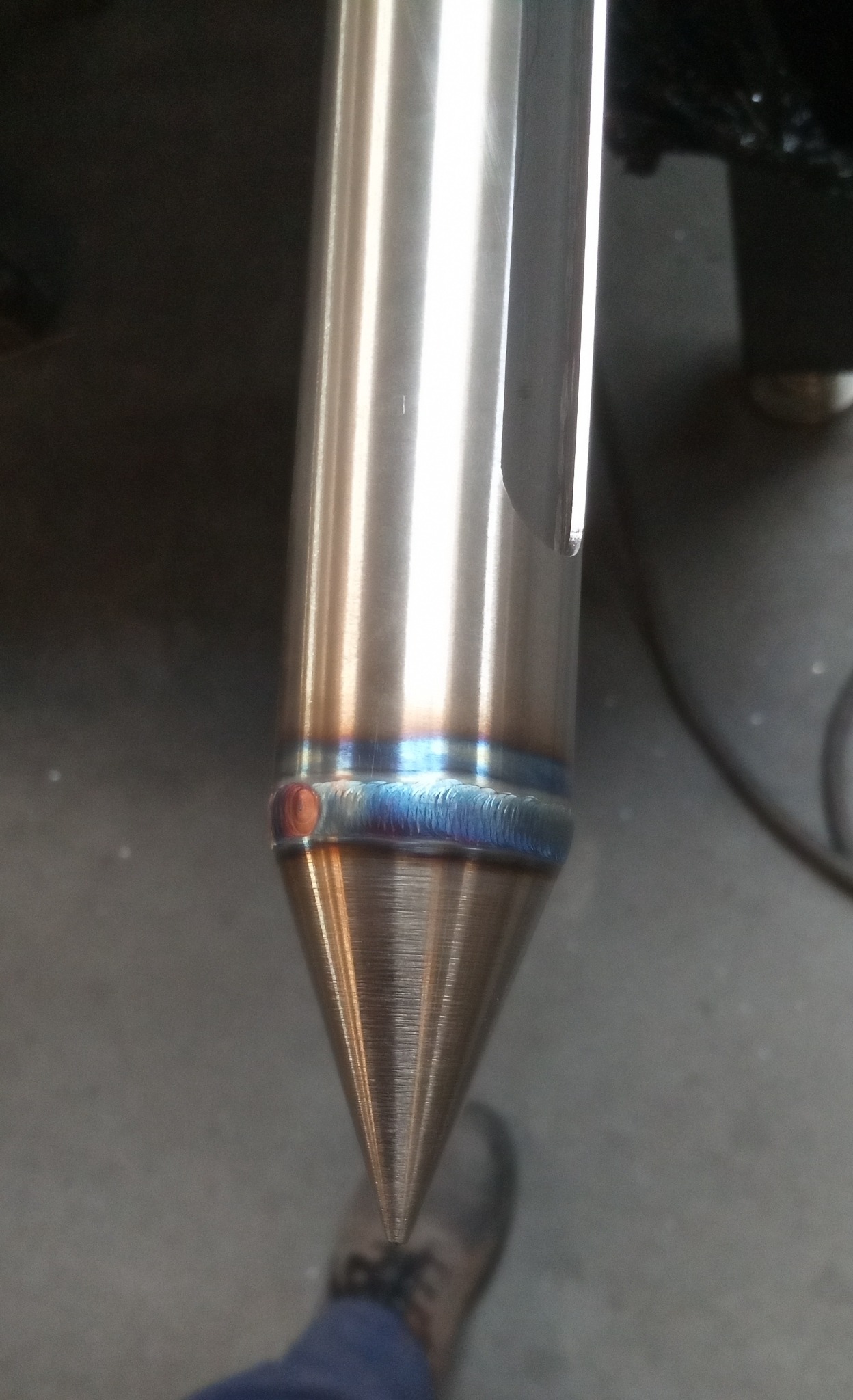 Precyzyjny spaw na stożkowym elemencie ze stali nierdzewnej, widoczne charakterystyczne przebarwienia po spawaniu TIG. Szlifowana powierzchnia, detal z bliska.