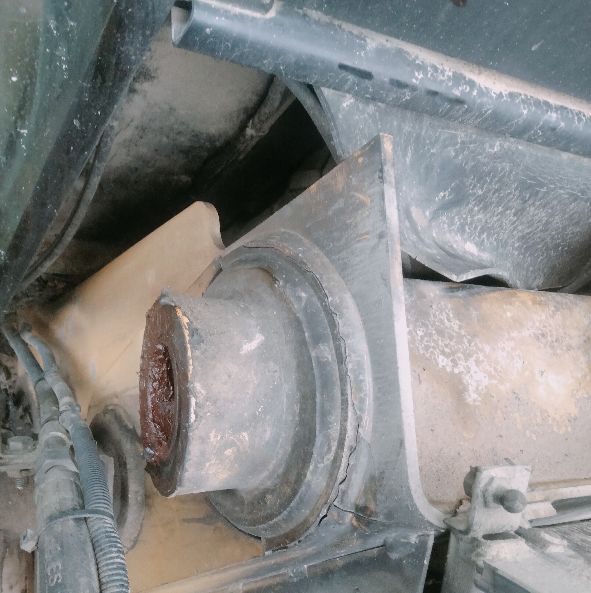 Szare, metalowe elementy konstrukcyjne z widocznymi śladami użytkowania i smarowania, fragment instalacji z przewodami w tle, ujęcie z dołu.