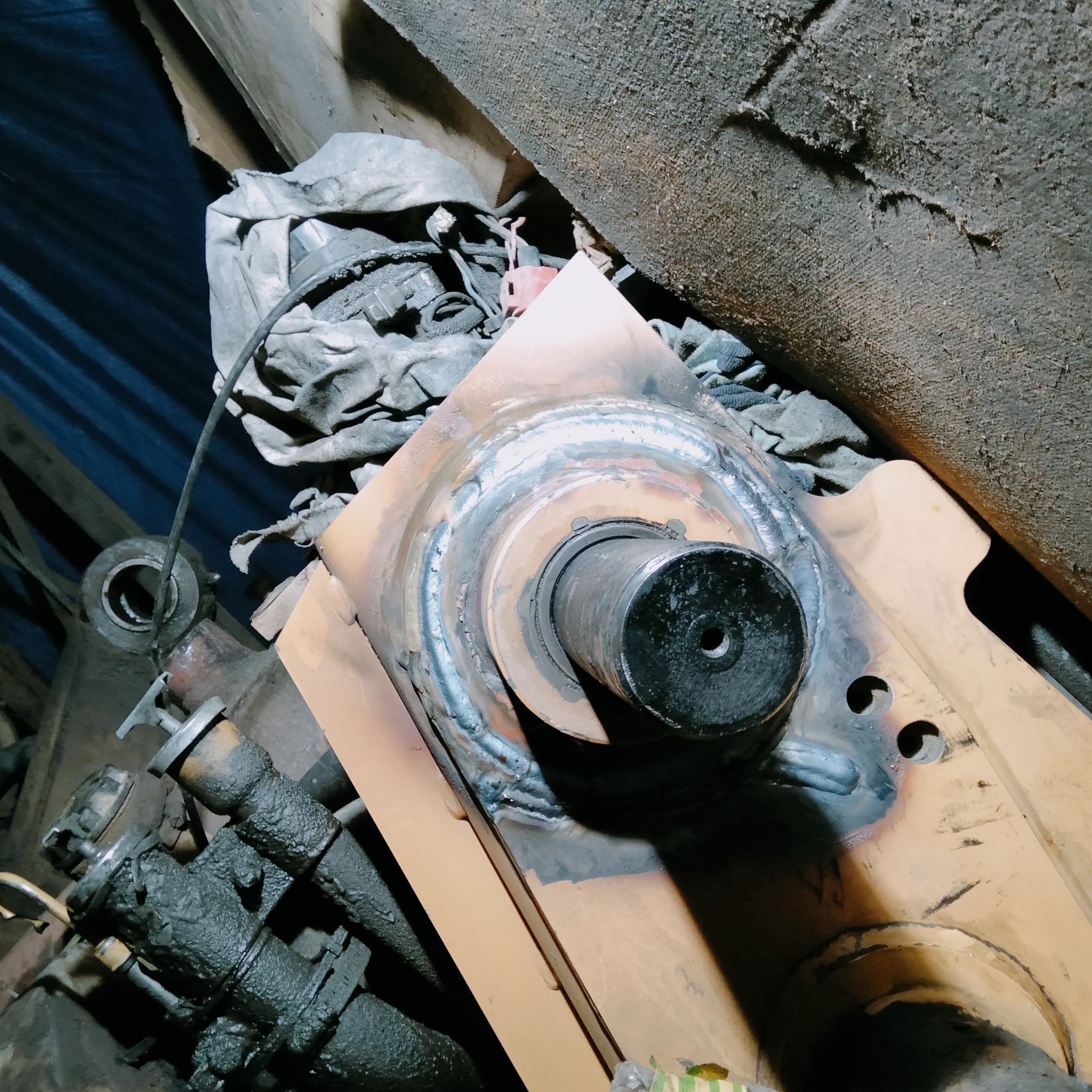 Żółty element konstrukcyjny po spawaniu z widocznymi śladami spawów, otoczony innymi metalowymi elementami i narzędziami w warsztacie.