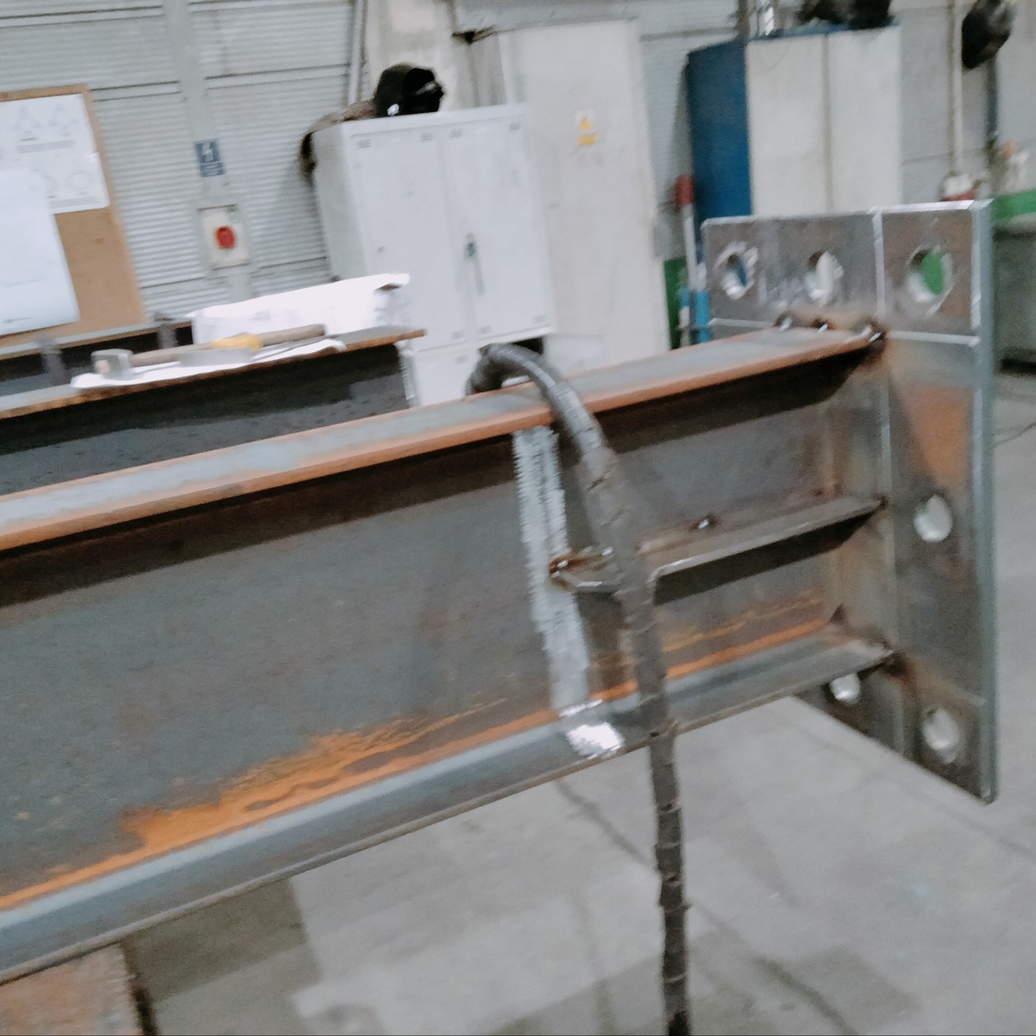 Surowa, spawana konstrukcja stalowa z otworami, widoczne ślady spawania i rdzy, w tle warsztat. Element konstrukcyjny przed malowaniem.