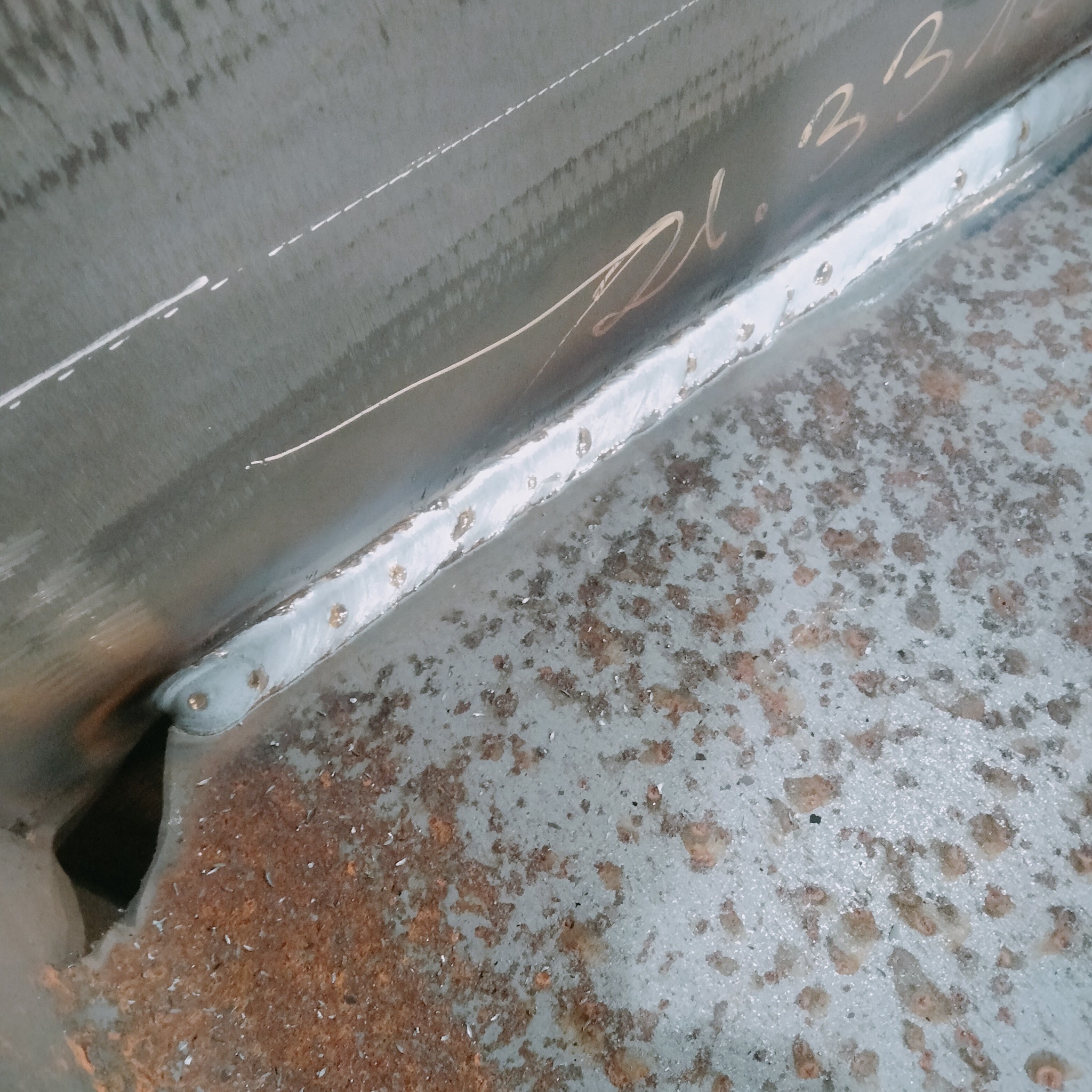 Spoina łącząca dwie metalowe płyty, widoczne ślady spawania i numer seryjny na metalu. Szlifowana powierzchnia z rdzawymi plamami.