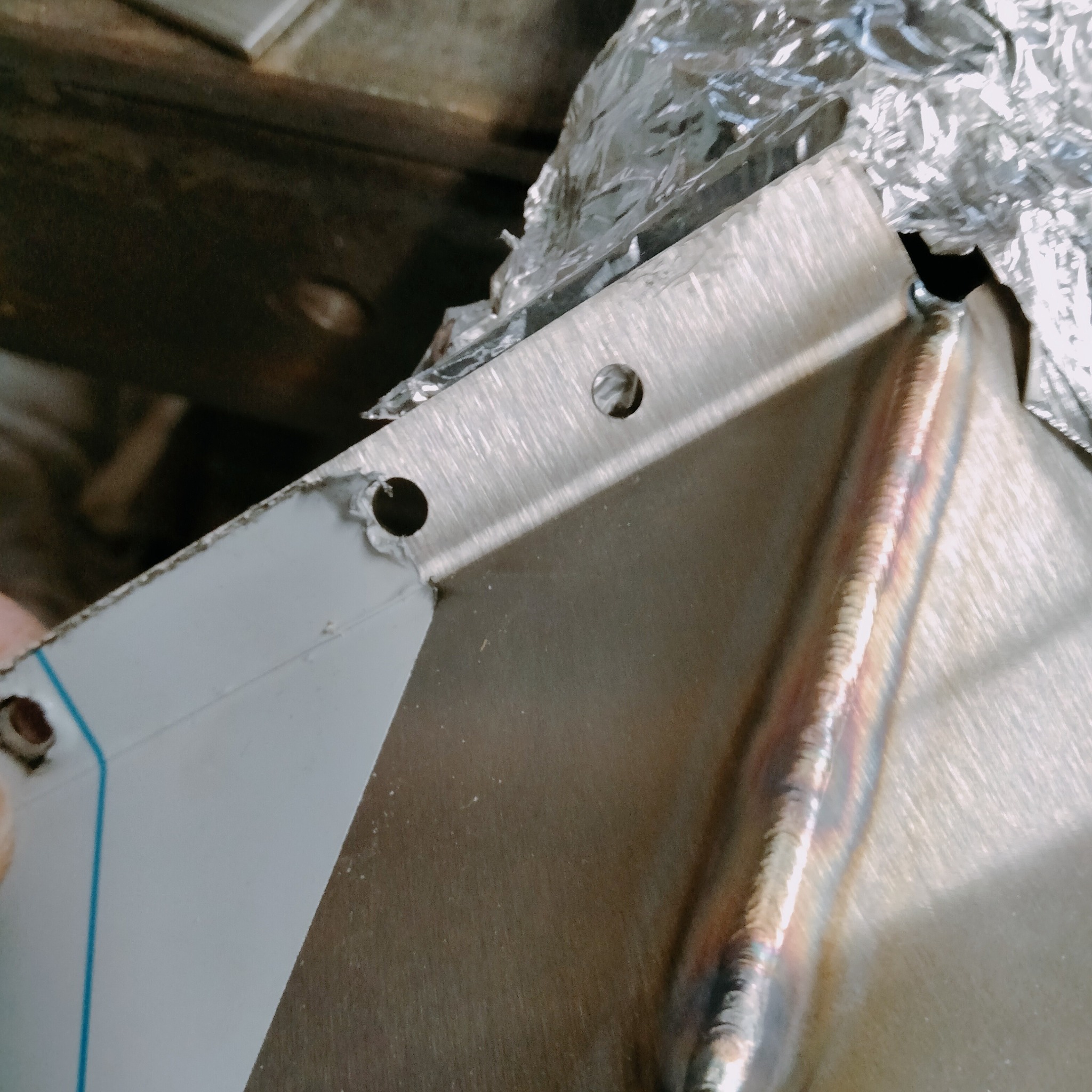 Szlifowany metal z widocznym spoiwem po spawaniu i otworami, zabezpieczony folią. Detal konstrukcyjny po obróbce, gotowy do dalszego montażu.