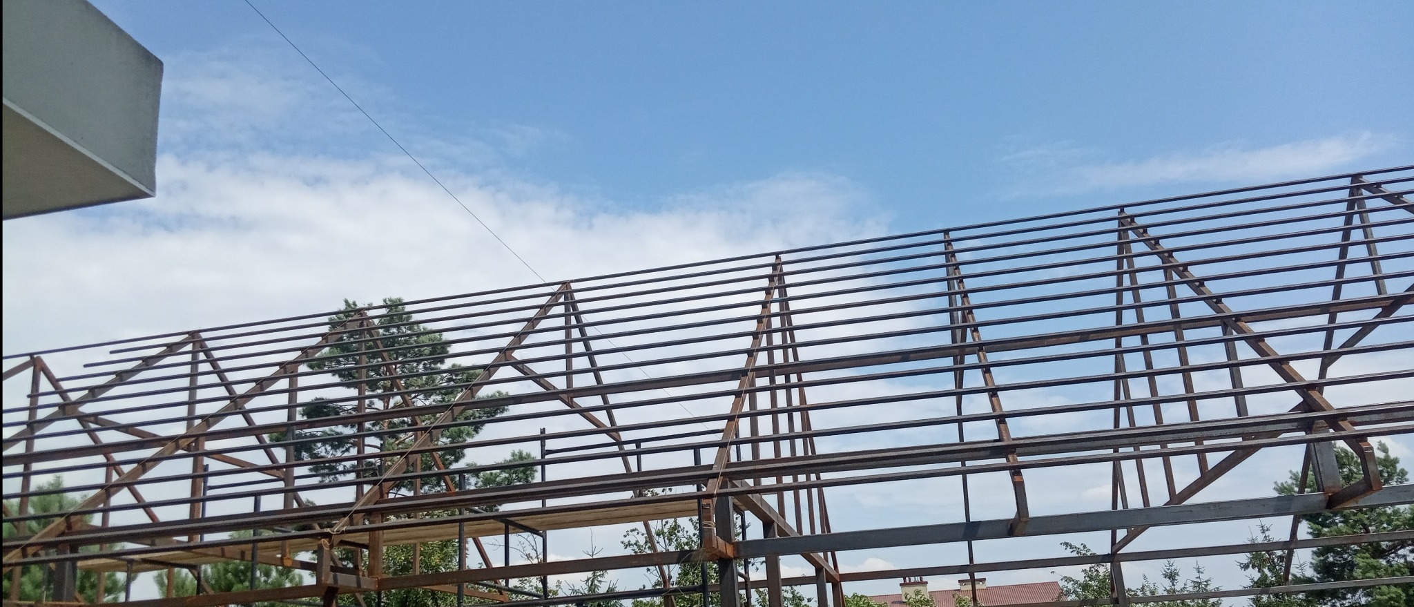 Konstrukcja stalowa dachu w Woli Zgłobieńskiej, widok od dołu na tle błękitnego nieba z chmurami. Elementy spawane, surowy metal.