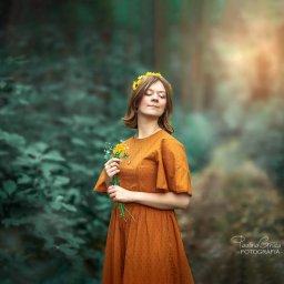 Paulina Gruca - Portret młodej kobiety z zamkniętymi oczami, w pomarańczowej sukience i wianku z żółtych kwiatów, trzymającej bukiecik polnych kwiatów na tle leśnej scenerii.