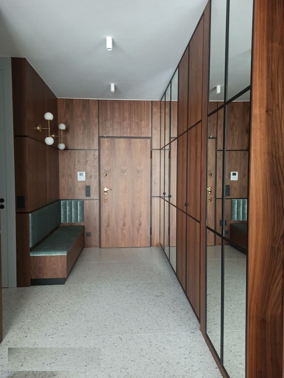 Nowoczesny przedpokój z drewnianą zabudową, lustrami w czarnych ramach, wbudowaną ławką z zielonym siedziskiem i podłogą z lastryko.