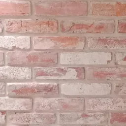 Tekstura ściany z cegły w odcieniach różu i bieli, imitująca starą, odrapaną powierzchnię.
