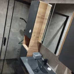 Nowoczesna łazienka z kabiną prysznicową typu walk-in, umywalką w kolorze grafitowym i szafką z drewnianymi elementami oraz czarną armaturą.