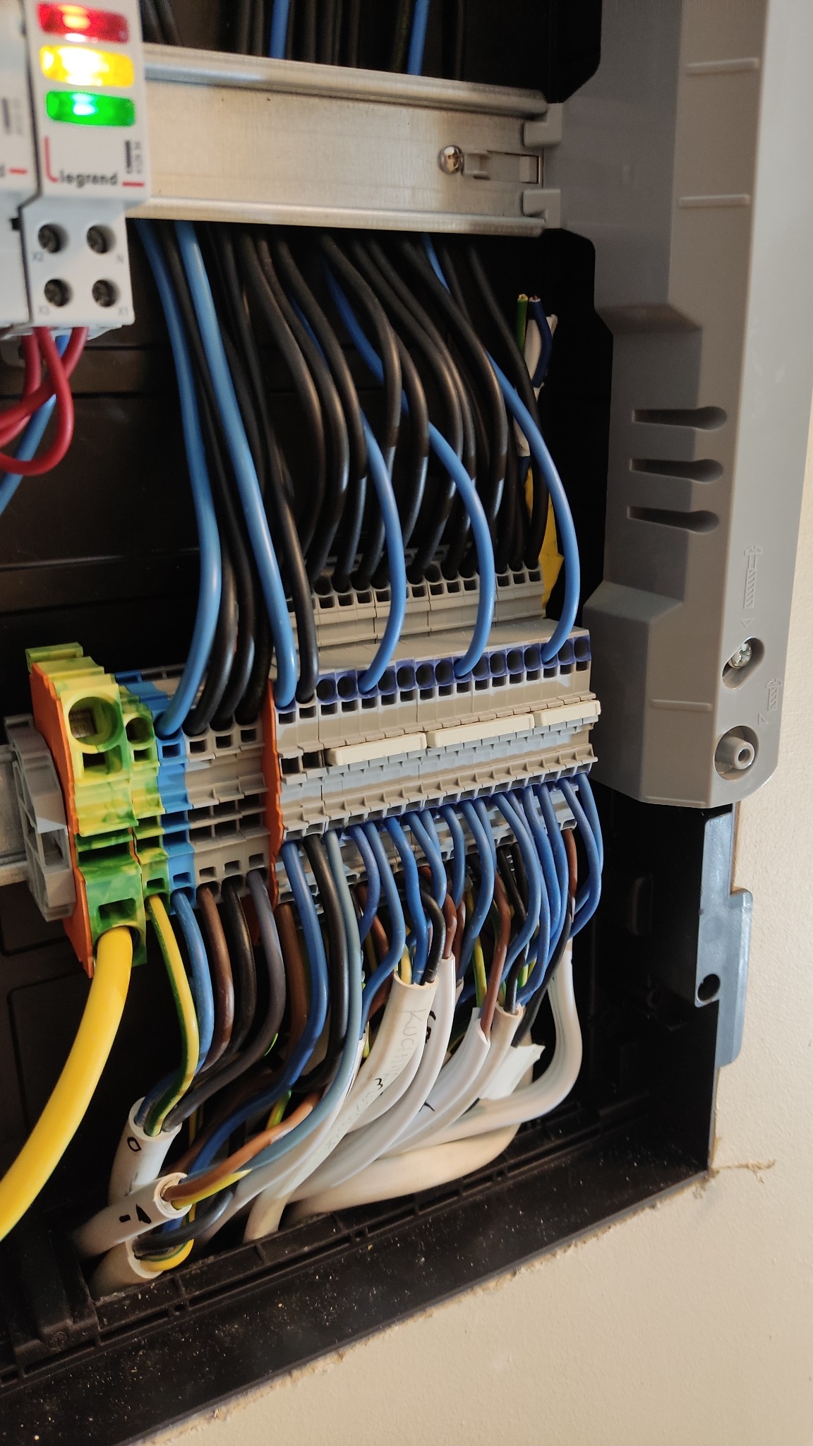 Szczegółowe ujęcie rozdzielnicy elektrycznej z podłączonymi przewodami o różnych kolorach (niebieski, czarny, biały, brązowy, żółty) i złączkami TOP JOB S, widoczne oznaczenia na przewodach.