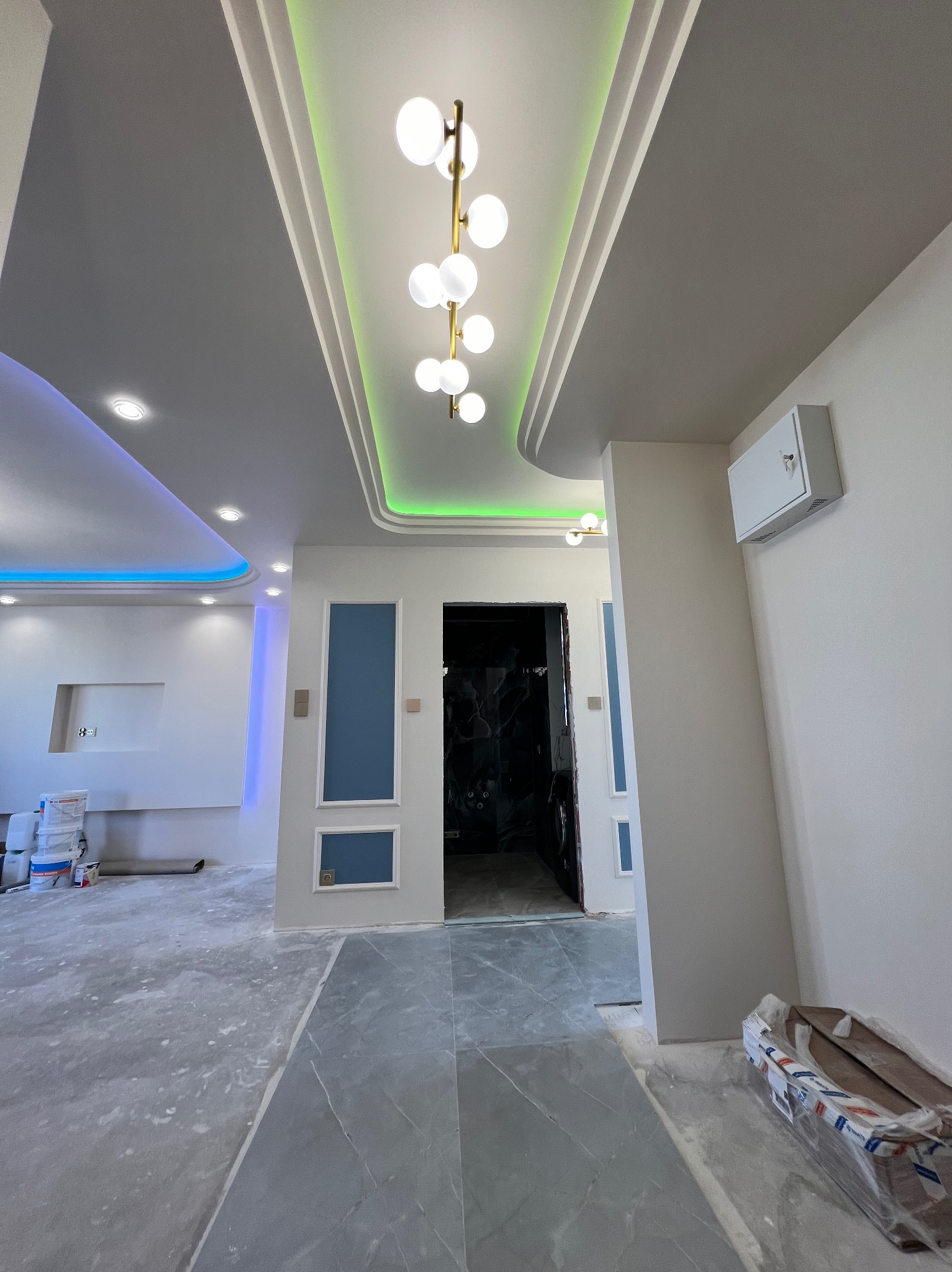 Nowoczesne wnętrze w trakcie prac wykończeniowych: sufit z podświetleniem LED, marmurowa podłoga i pomalowane ściany. Widoczne puszki z farbą i materiały budowlane.