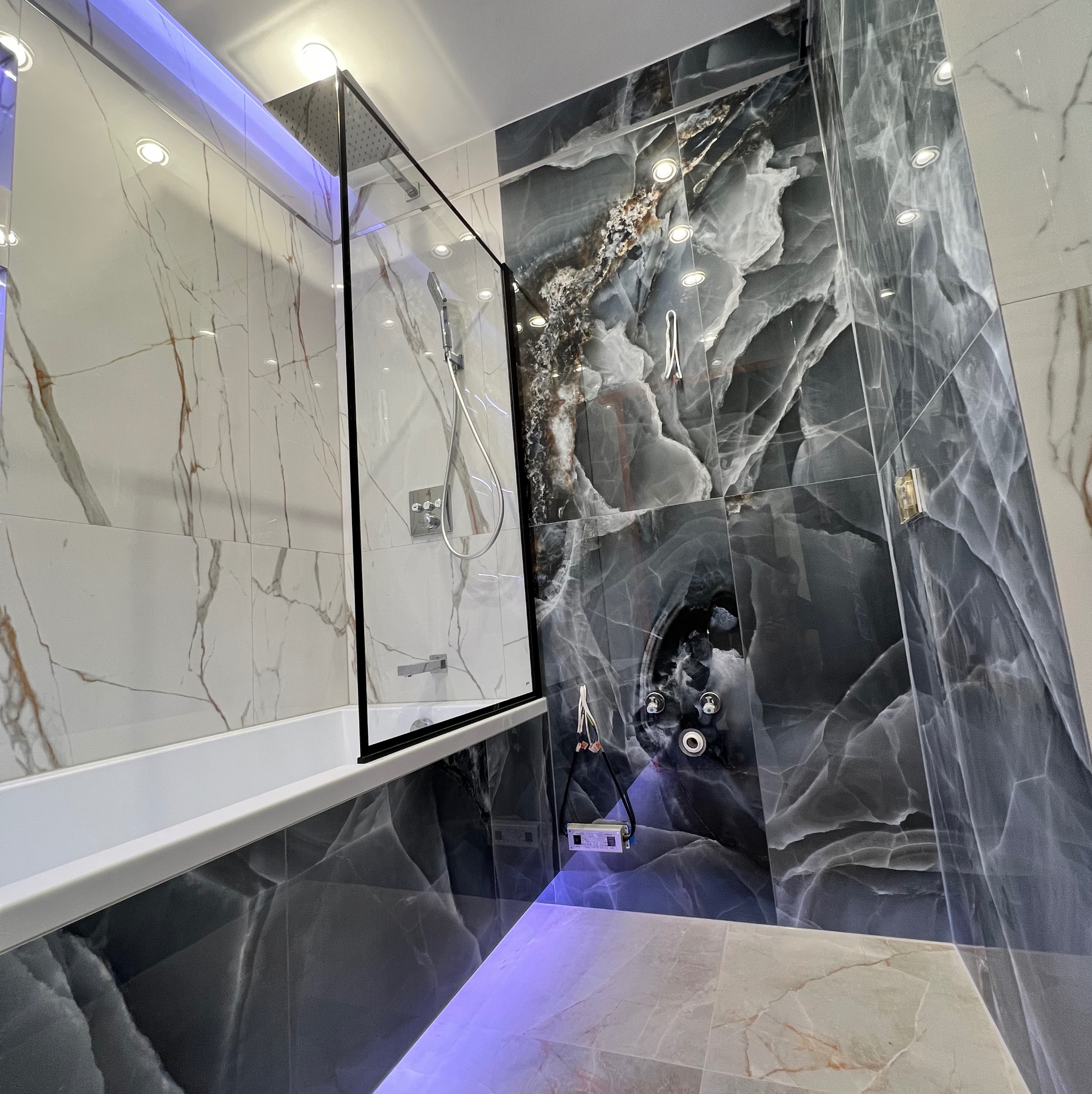 Nowoczesna łazienka w Warszawie z kabiną prysznicową typu walk-in, wykończona płytkami imitującymi marmur w odcieniach szarości i bieli, z subtelnym podświetleniem LED podkreślającym luksusowy...