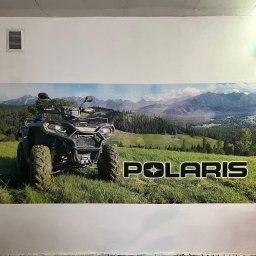 Future Design - Duży plakat z pojazdem ATV marki Polaris na tle górskiego krajobrazu, naklejony na białej ścianie w pomieszczeniu z surowym wykończeniem.
