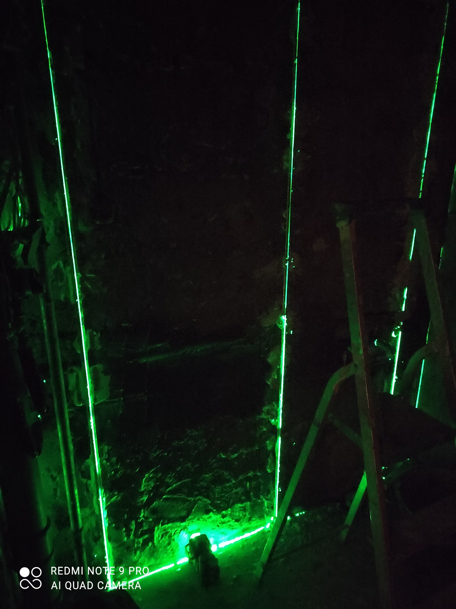 Zielone linie lasera wyznaczają pion i poziom na surowej ścianie podczas prac remontowych, widoczna drabina.