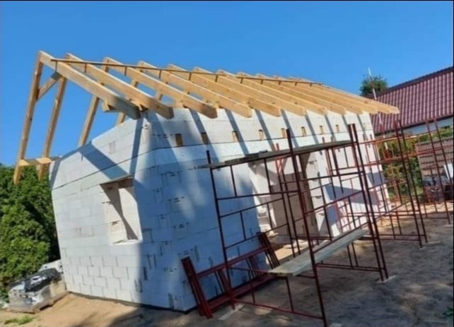 Budowa domu jednorodzinnego z bloczków, widoczna drewniana konstrukcja dachu i rusztowania.