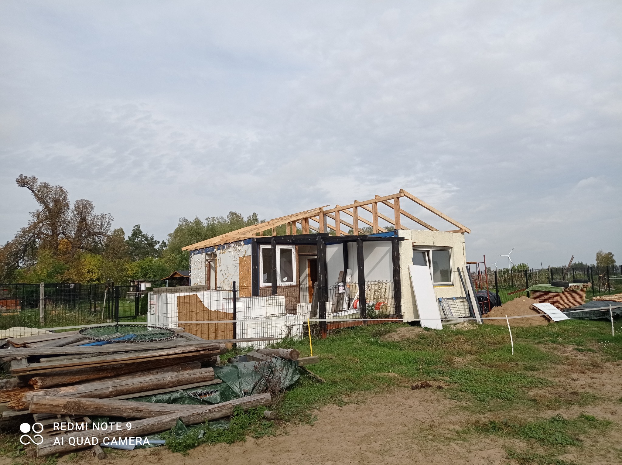 W trakcie budowy domu w Nakle nad Notecią: widoczna konstrukcja więźby dachowej, ściany w trakcie ocieplania, porozrzucane materiały budowlane i teren wokół w trakcie zagospodarowywania.