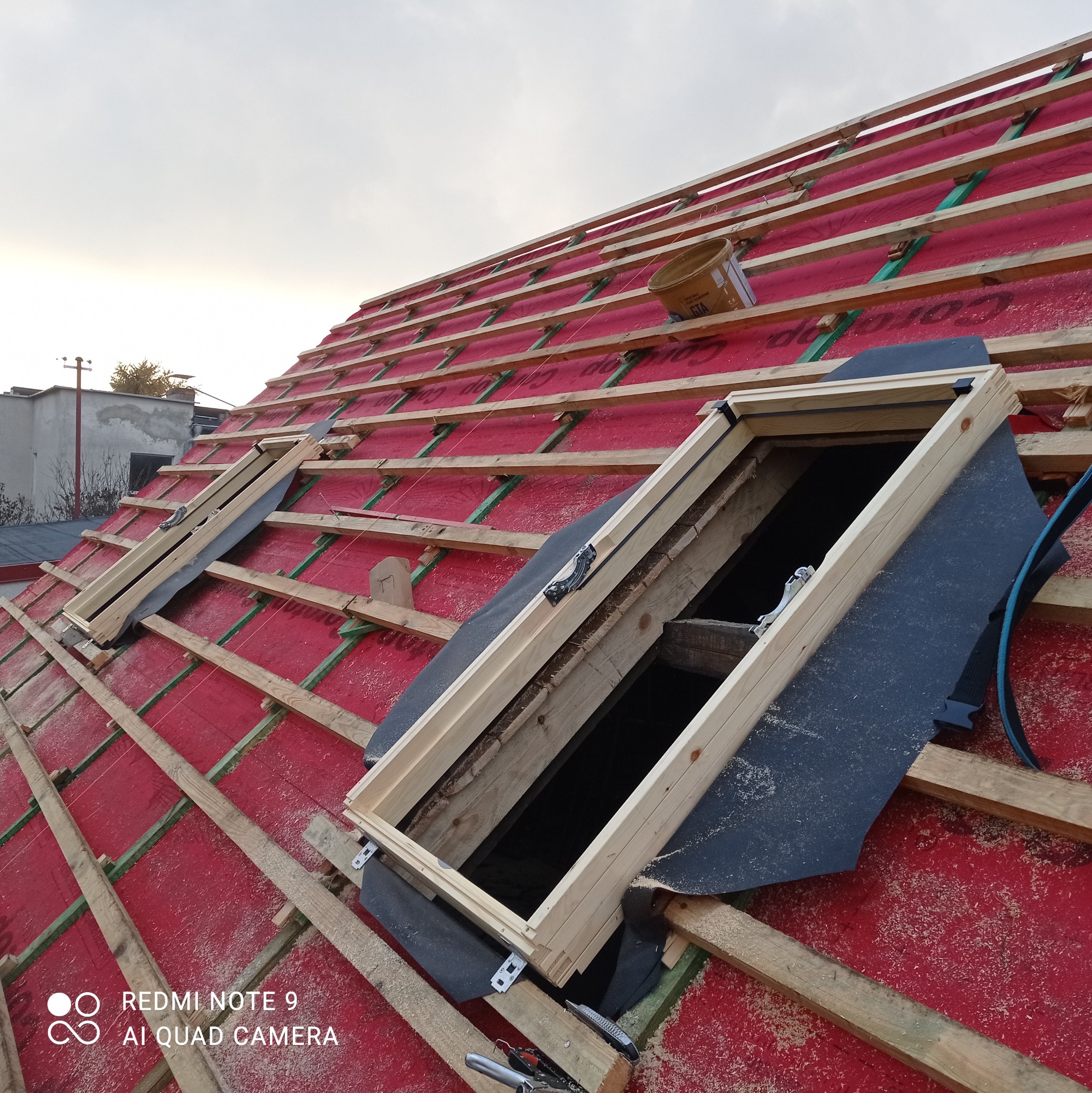 W trakcie montażu okien dachowych na czerwonej membranie dachowej z widoczną konstrukcją drewnianą i elementami mocującymi.