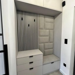 Rafał Grządziel RAFMEB Usługi Stolarskie - Wnęka w przedpokoju z siedziskiem, tapicerowanym panelem ściennym, szafkami z szufladami i wieszakami w czarno-białe paski.