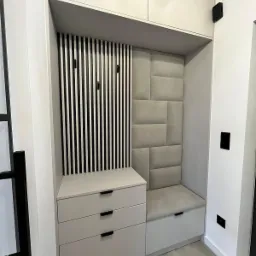 Wnęka w przedpokoju z siedziskiem, tapicerowanym panelem ściennym, szafkami z szufladami i wieszakami w czarno-białe paski.