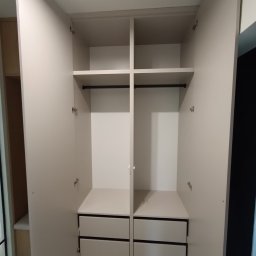 Rafał Grządziel RAFMEB Usługi Stolarskie - Otwarta szafa wnękowa z szufladami i półkami, widoczne zawiasy na drzwiach, jasne wykończenie.