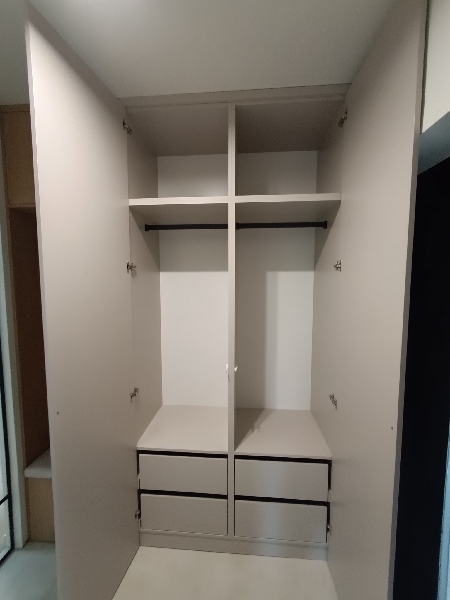 Otwarta szafa wnękowa z szufladami i półkami, widoczne zawiasy na drzwiach, jasne wykończenie.