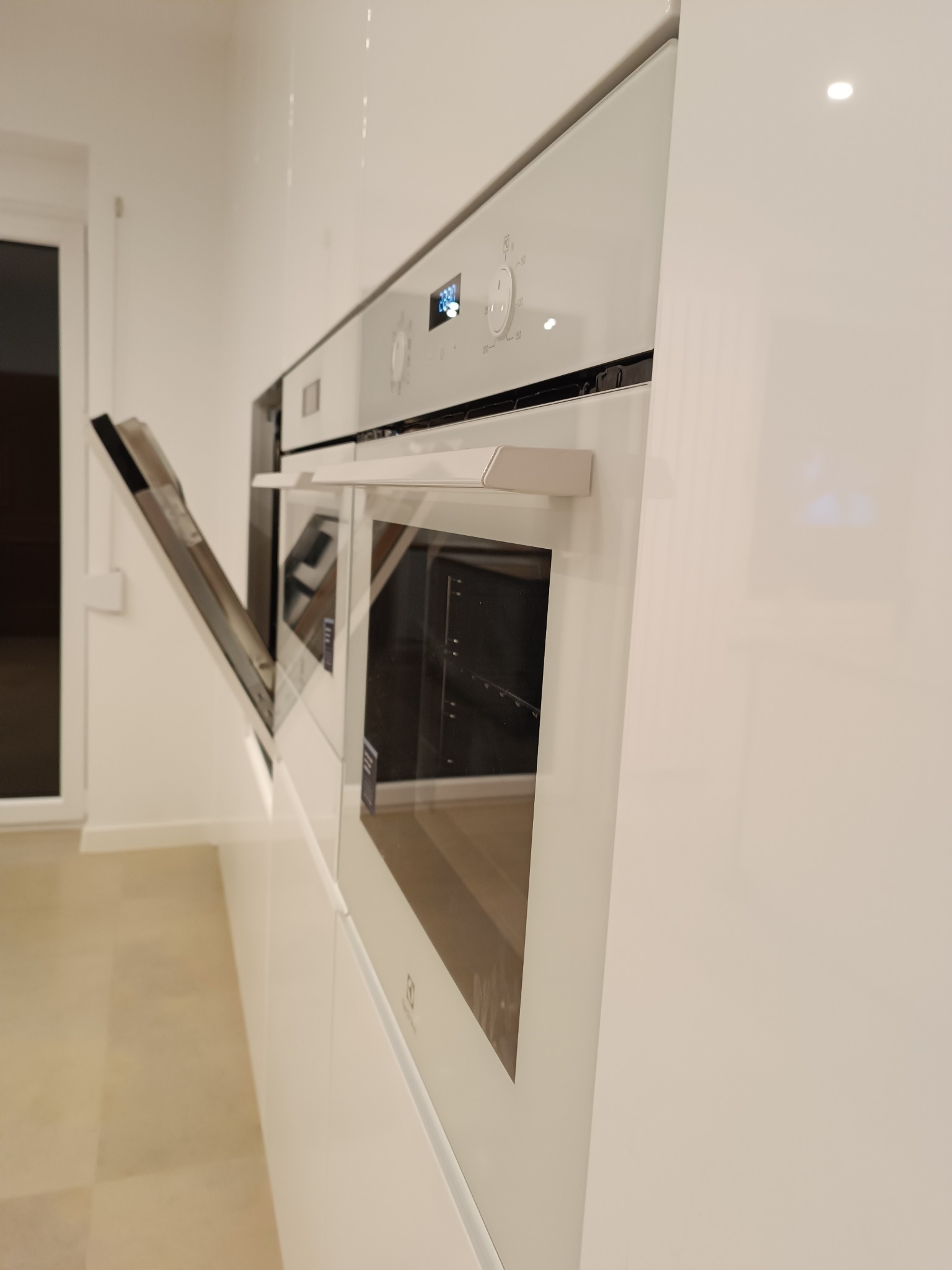 Biała zabudowa kuchenna z piekarnikiem Electrolux, otwarte drzwiczki. Minimalistyczny design, gładkie fronty, nowoczesne oświetlenie. Detal kuchni na wymiar.