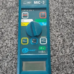 Miernik Sonel MIC-3 do pomiarów elektrycznych, z podłączonymi przewodami, leżący na szarej, nakrapianej powierzchni.