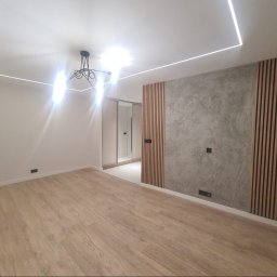 Damian Konopka - Nowoczesne wnętrze po remoncie: drewniana podłoga, ściana z dekoracyjnym betonem i drewnianymi lamelami, oświetlenie LED na suficie. Minimalistyczny design.