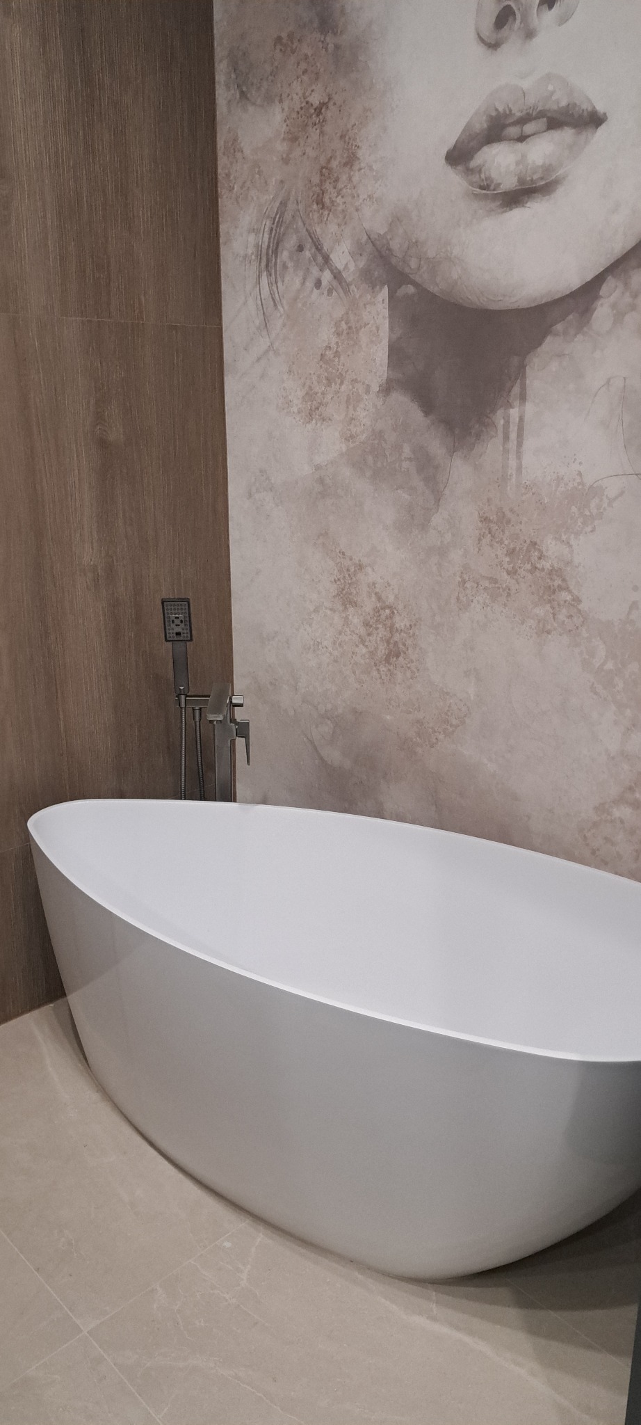 Nowoczesna, wolnostojąca wanna owalna z chromowaną armaturą na tle ściany z efektem akwareli i drewnopodobnej okładziny. Minimalistyczny design łazienki.