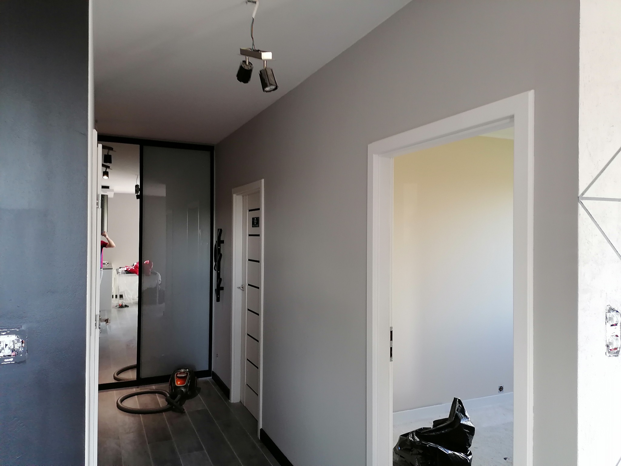 Korytarz w Borkowie po odświeżeniu, z szarymi ścianami, drewnianą podłogą i minimalistycznym oświetleniem; widoczny odkurzacz i worki na śmieci sugerują prace wykończeniowe.