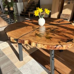 Studio Dekoracji Wnętrz Forrest - Okrągły blat drewniany z żywicą na metalowych nogach, wykończony na surowo, z wazonem żółtych kwiatów. W tle schody i elementy wystroju wnętrza.