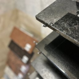 Studio Dekoracji Wnętrz Forrest - Ekspozycja próbek blatów z konglomeratu w różnych kolorach i fakturach, z bliska, z widocznymi detalami wykończenia krawędzi i strukturą materiału.