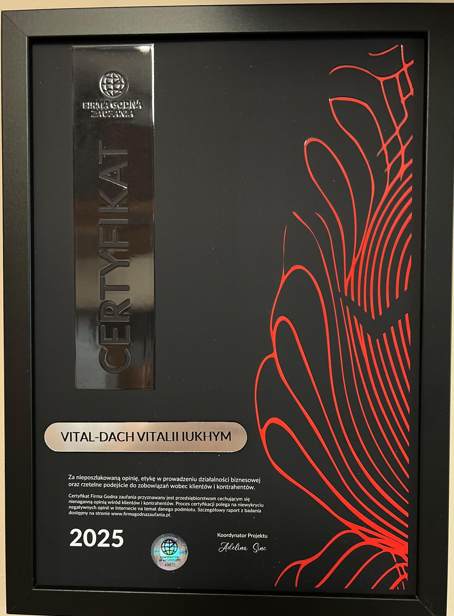 Oprawiony certyfikat 'Firma Godna Zaufania' dla VITAL-DACH VITALII IUKHYM, ważny do 2025 roku. Czerwone, abstrakcyjne zdobienia na czarnym tle.