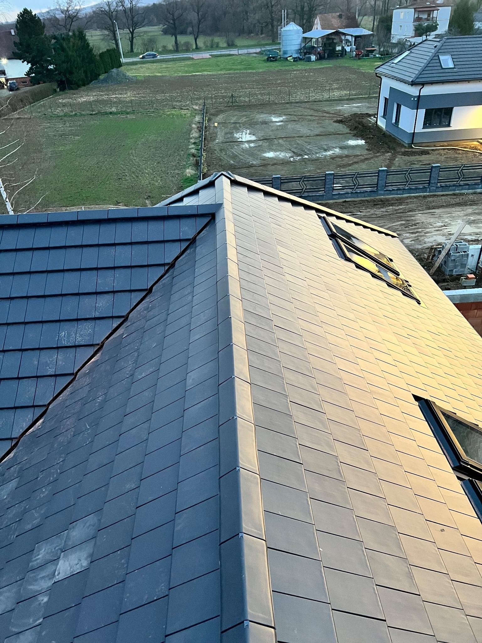 Nowoczesny dach z dachówką ceramiczną w odcieniach szarości, z oknami dachowymi, wykonany przez dekarza we Wrocławiu. Widok z góry na ukończony projekt.