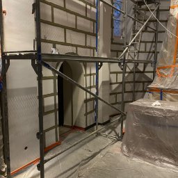 SASIUK SPÓŁKA Z OGRANICZONĄ ODPOWIEDZIALNOŚCIĄ - Wnętrze w trakcie remontu, ściany z nałożonymi płytami kartonowo-gipsowymi imitującymi cegłę, widoczne rusztowania i zabezpieczenia folią.