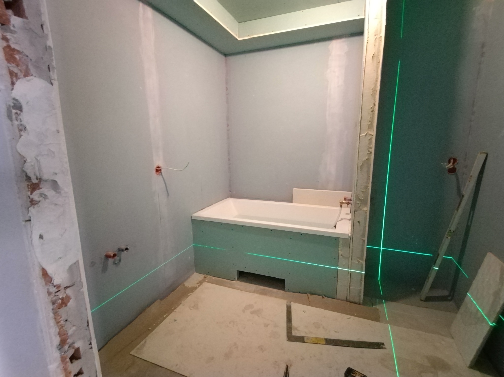 Łazienka w trakcie prac wykończeniowych; widoczna wanna obudowana płytami gipsowo-kartonowymi, ściany przygotowane pod malowanie, poziomica laserowa wyznacza linie proste, surowy stan wykończenia.