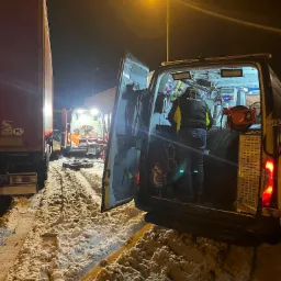 Mechanik w pojeździe serwisowym przy drodze, prawdopodobnie wymiana opon ciężarówki w warunkach zimowych, widoczne narzędzia i opony wewnątrz pojazdu, śnieg na poboczu.