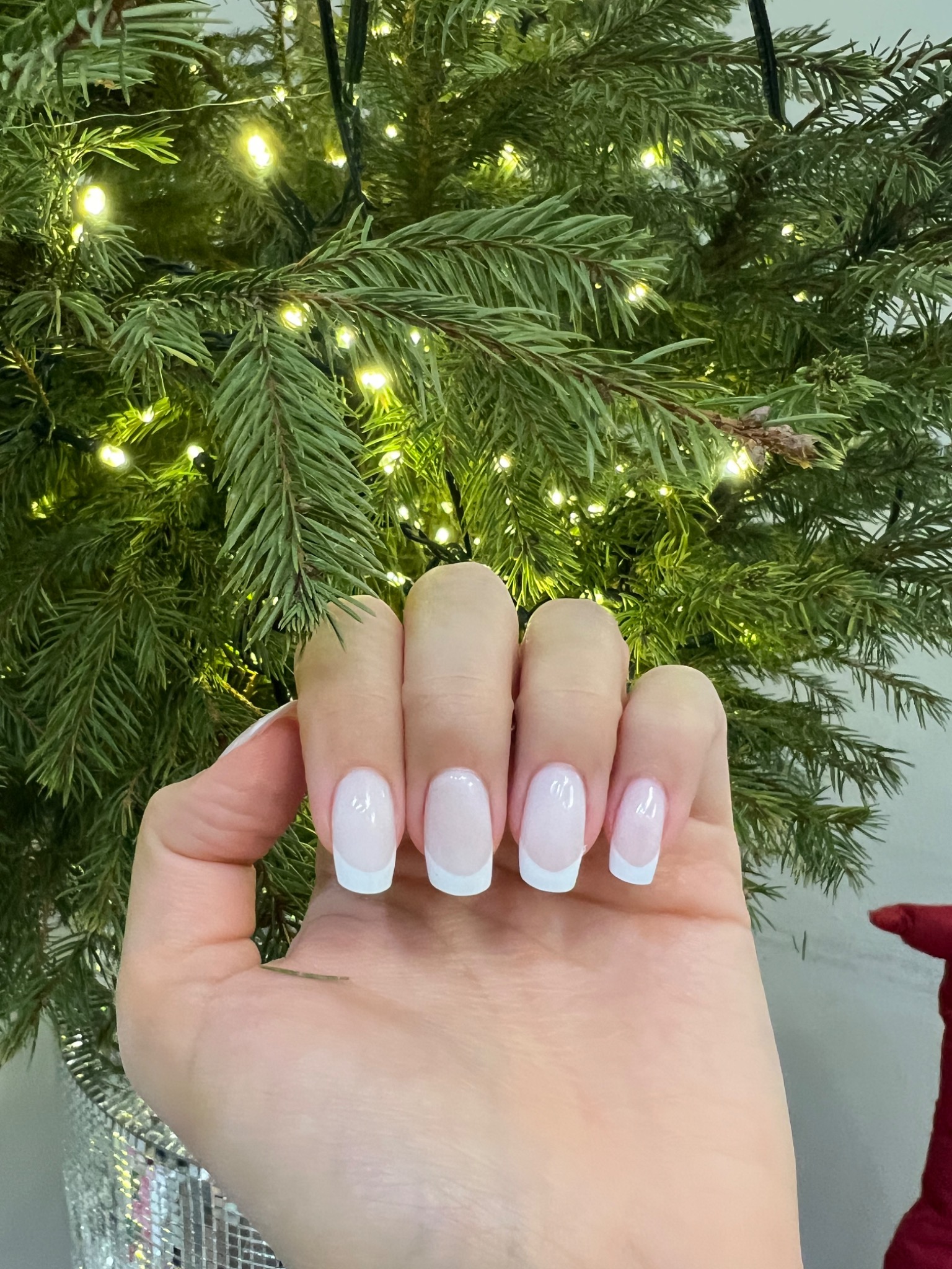 Dłoń z białym, francuskim zdobieniem paznokci na tle choinki z lampkami