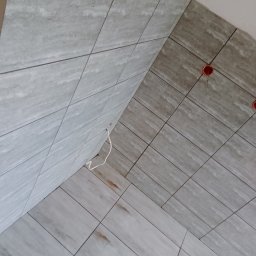 My House recovery - Ułożone jasnoszare płytki imitujące drewno na ścianie i podłodze w rogu pomieszczenia, widoczne puszki elektryczne i wystający przewód.