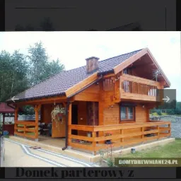 Gotowy parterowy dom z bali z brązowym dachem i drewnianą balustradą, widok z zewnątrz na tle drzew.