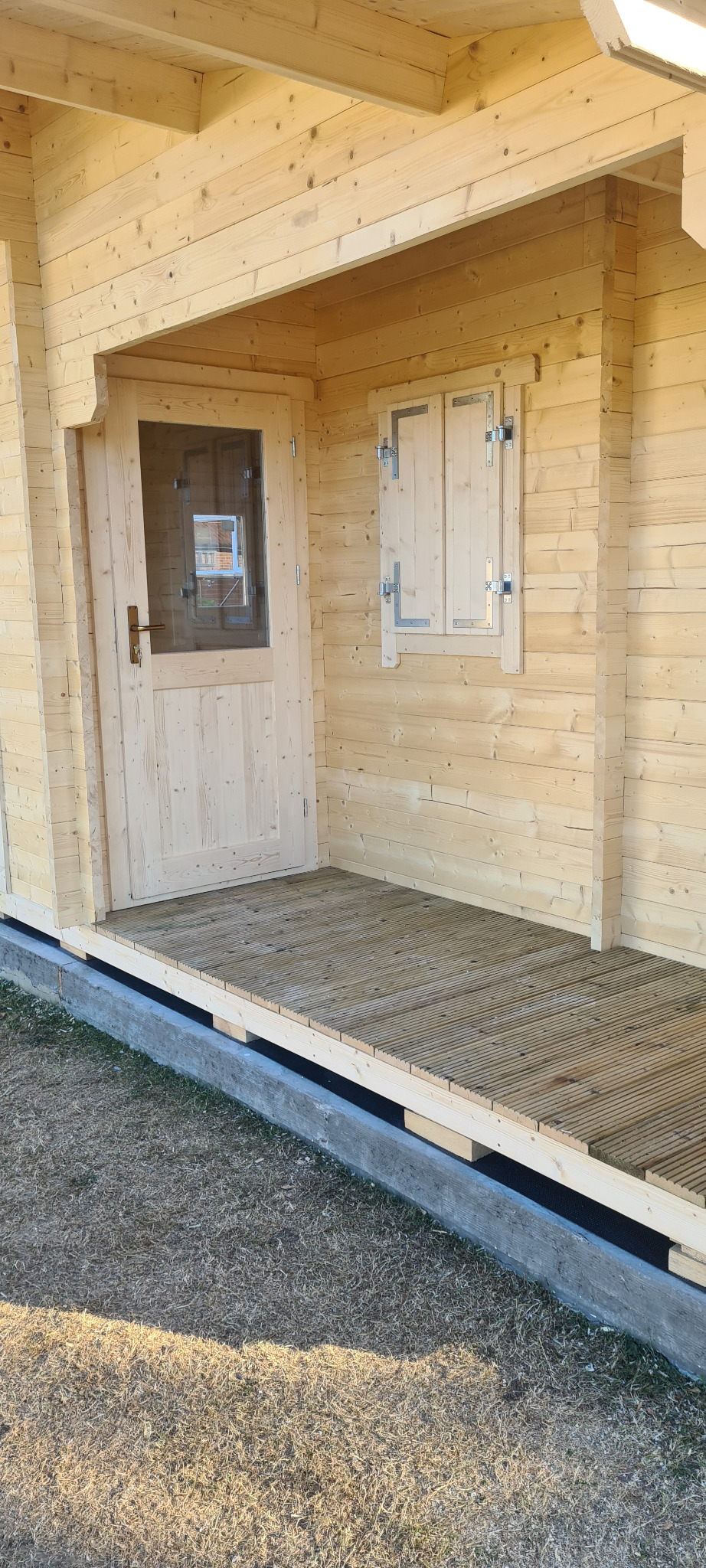 Surowa drewniana weranda z deskami i pojedynczym oknem z okiennicami, widok z zewnątrz.