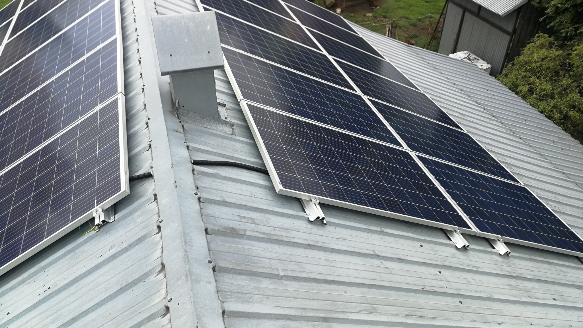 Panele fotowoltaiczne zamontowane na blaszanym dachu z widocznymi elementami mocującymi i rurą osłonową kabli.