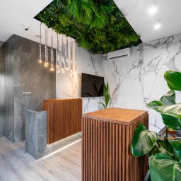 Manufactura - projektowanie wnętrz - Nowoczesne biuro z recepcją: drewniane panele, marmurowe ściany, zielona instalacja na suficie i designerskie oświetlenie. Minimalistyczny wystrój z roślinami.