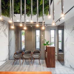 Manufactura - projektowanie wnętrz - Nowoczesne wnętrze biura z marmurowymi ścianami, drewnianą recepcją i zielonym sufitem. Trzy krzesła dla gości ustawione wzdłuż ściany z oknami.