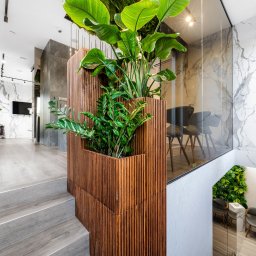 Manufactura - projektowanie wnętrz - Nowoczesne wnętrze z drewnianą ścianką działową, roślinami i marmurowymi wykończeniami. Widok z góry na schody i przestrzeń biurową z krzesłami.