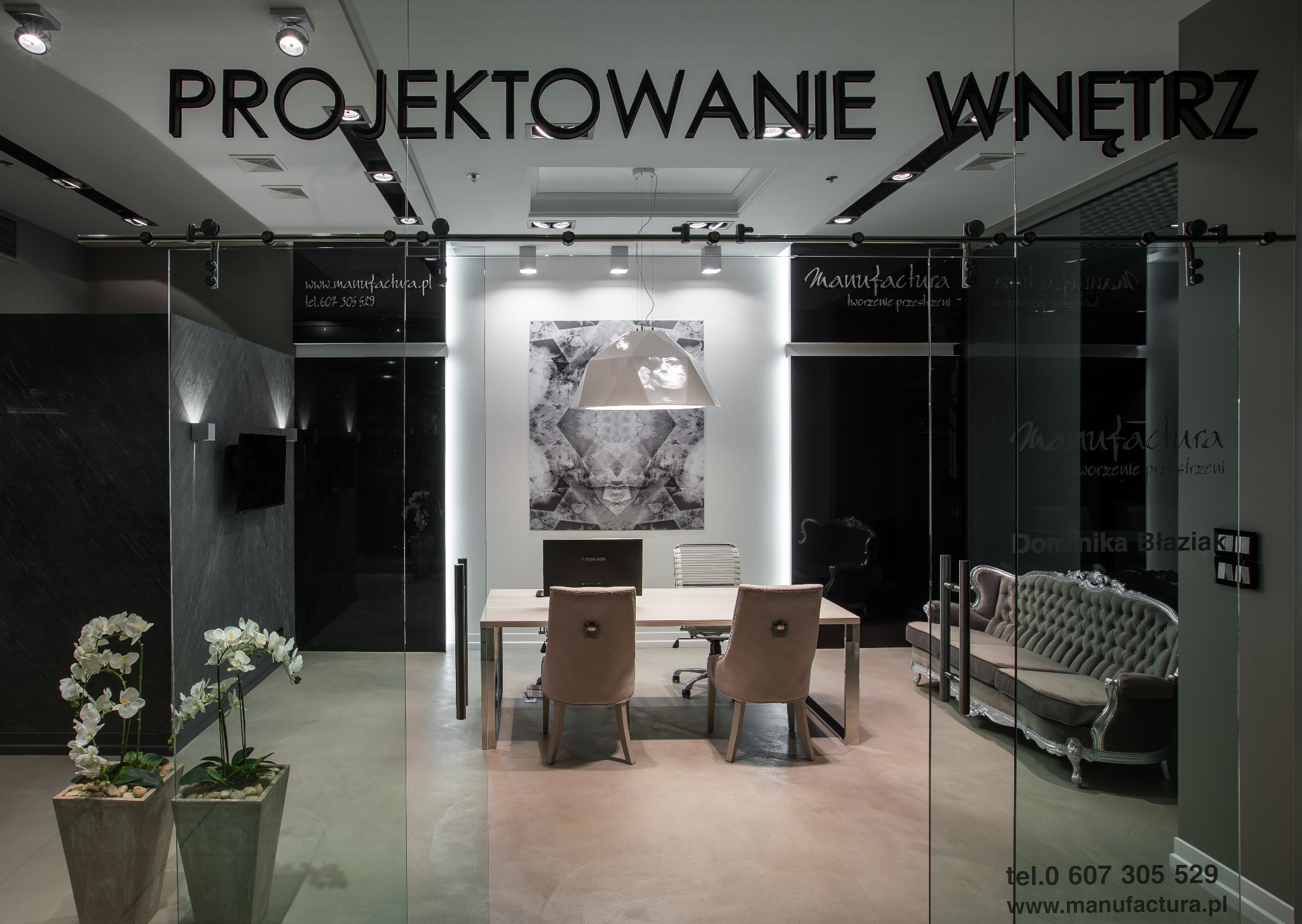 Eleganckie biuro projektowe z przeszklonymi drzwiami, widoczne biurko z komputerem, designerska lampa, sofa w stylu vintage i donica z orchideami, nad wejściem napis 'Projektowanie Wnętrz'.