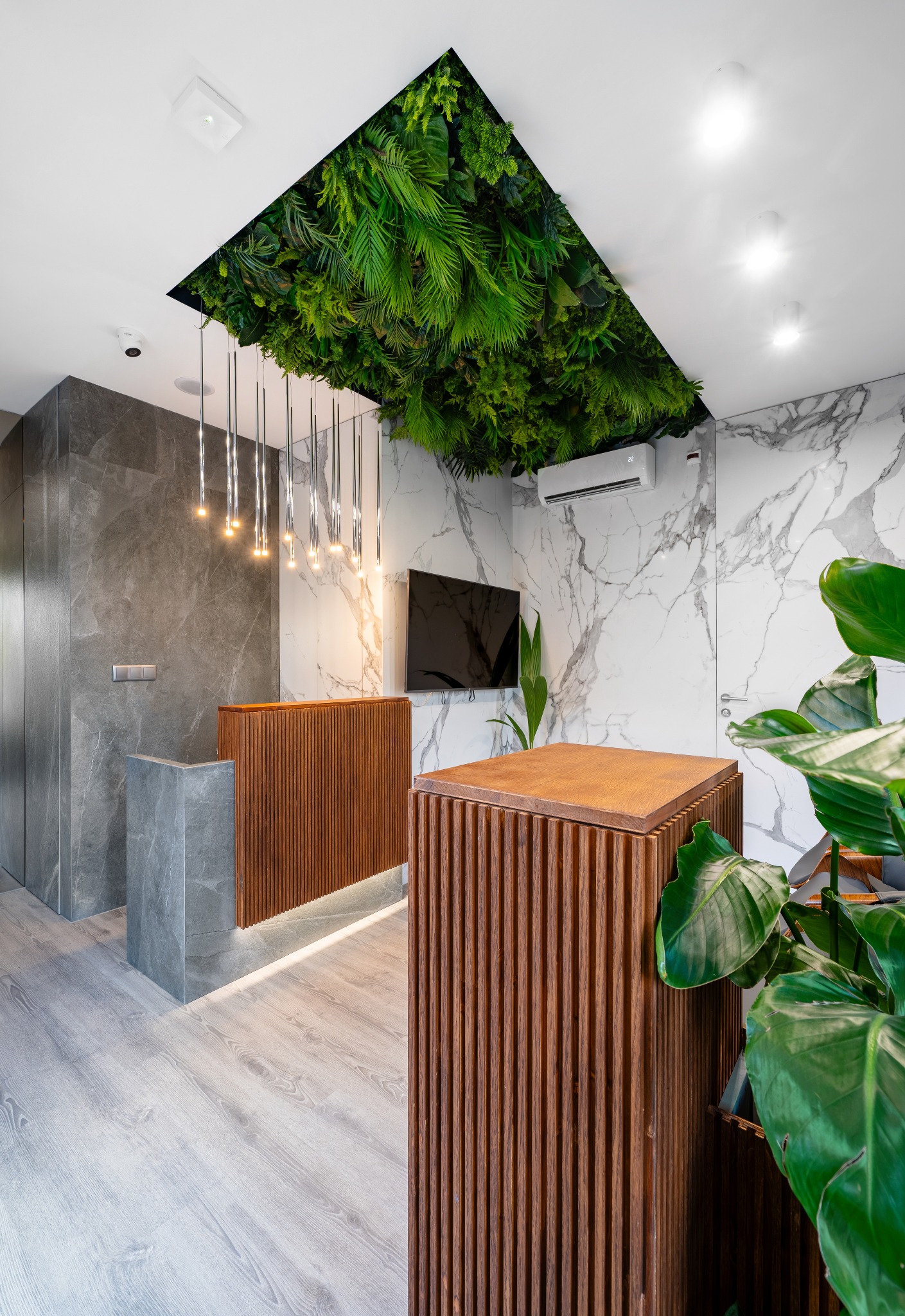 Nowoczesne biuro z recepcją: drewniane panele, marmurowe ściany, zielona instalacja na suficie i designerskie oświetlenie. Minimalistyczny wystrój z roślinami.