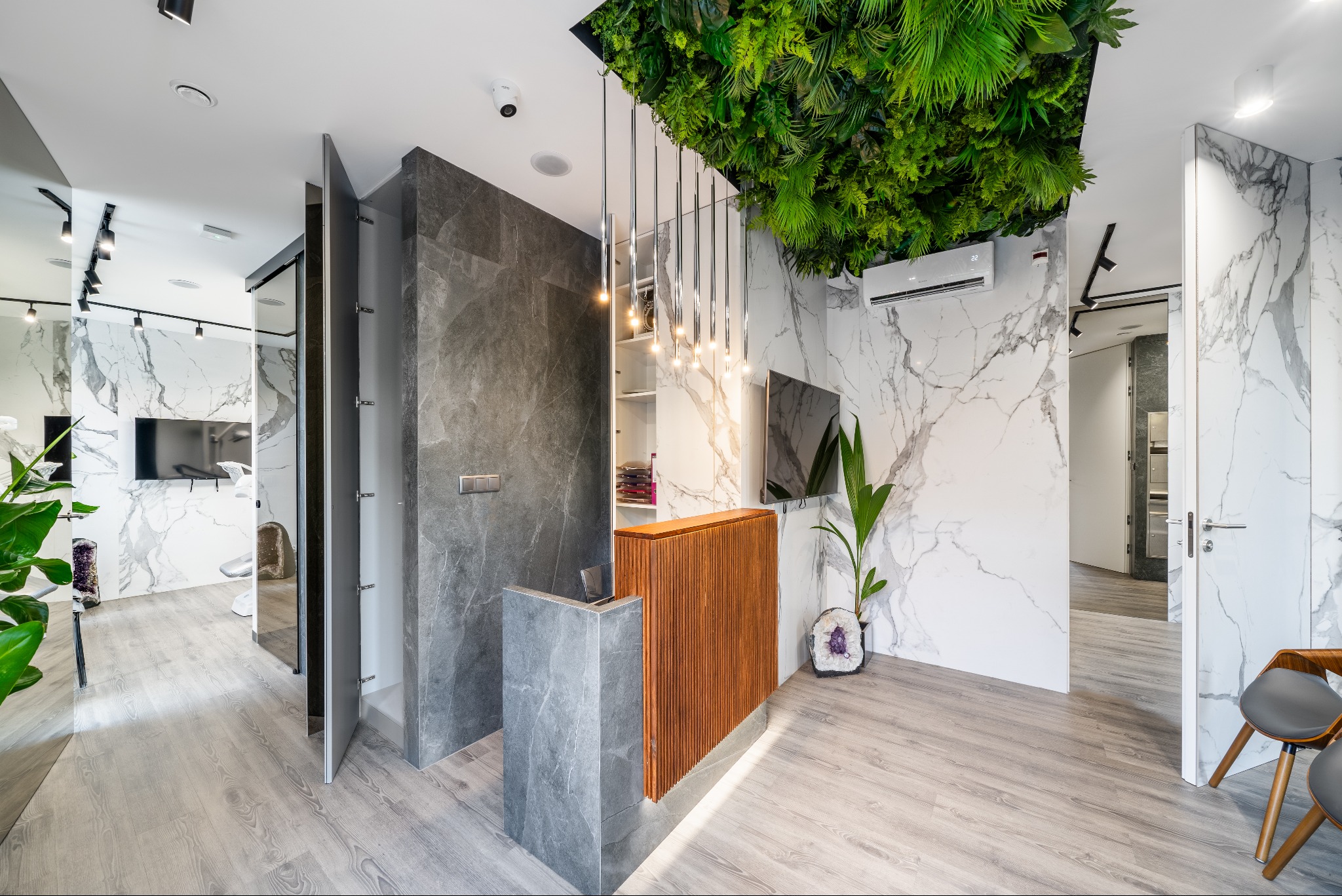 Nowoczesne biuro z recepcją: drewno, marmur, szarość i zieleń. Designerskie oświetlenie i rośliny tworzą unikalny klimat. Widok na gabinet zabiegowy.