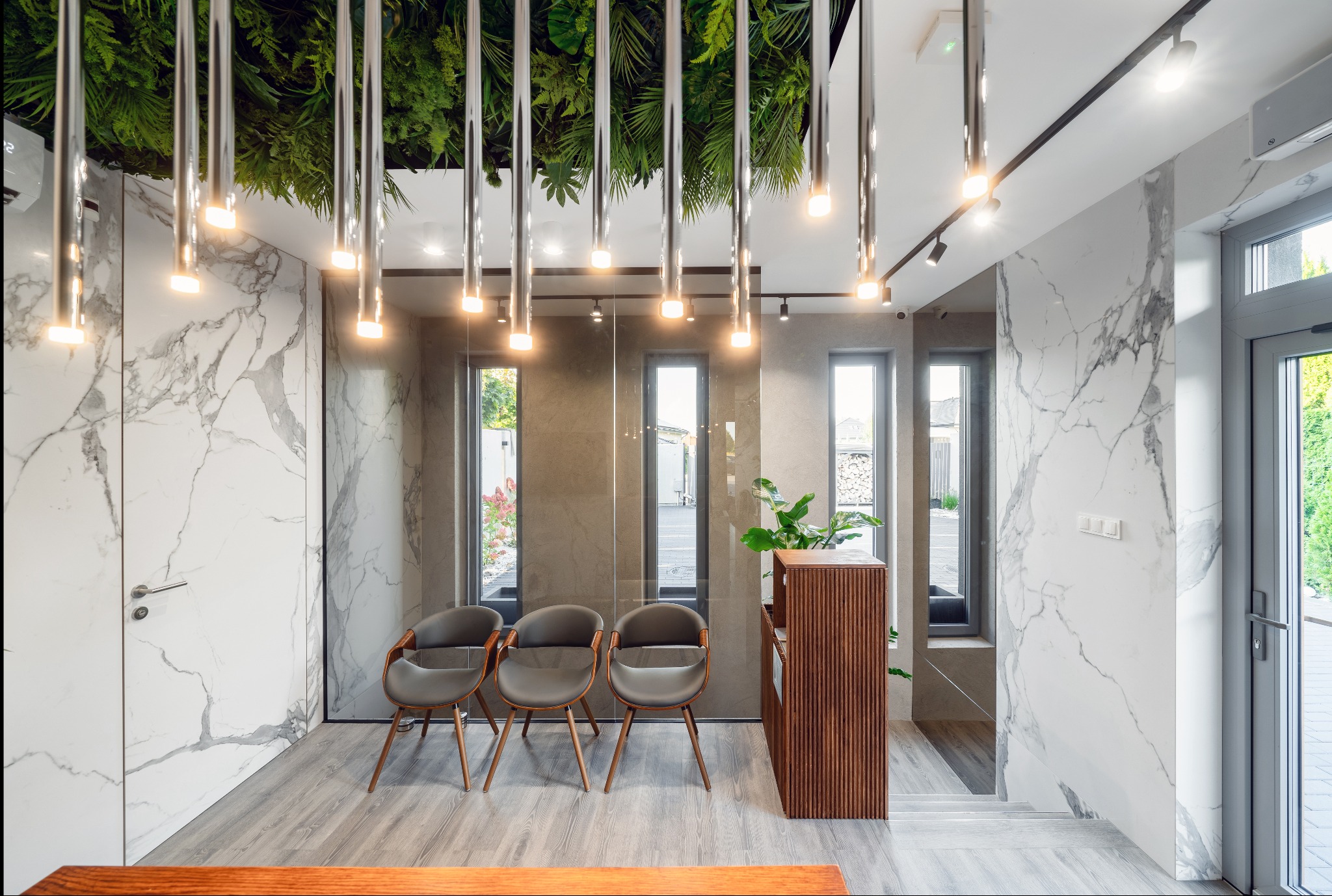 Nowoczesne wnętrze biura z marmurowymi ścianami, drewnianą recepcją i zielonym sufitem. Trzy krzesła dla gości ustawione wzdłuż ściany z oknami.