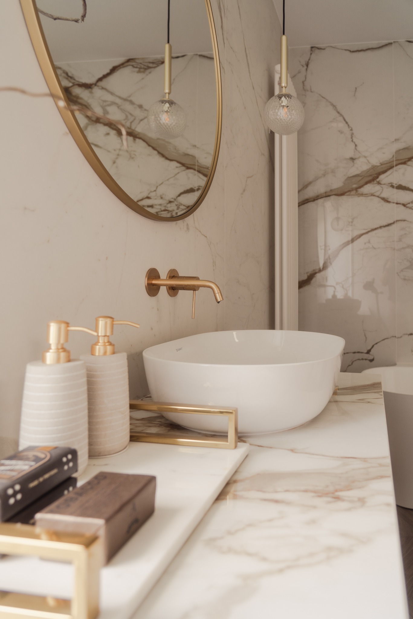 Elegancka łazienka z marmurową umywalką, złotą armaturą i okrągłym lustrem. Ciepłe oświetlenie podkreśla luksusowy charakter wnętrza.