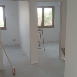 Set-Bud usługi remontowo-wykończeniowe - Wnętrze w trakcie wykończenia: białe ściany, wylewka, widoczne okna, drabina, szczotka i szufelka. Przygotowanie do malowania lub układania podłogi.
