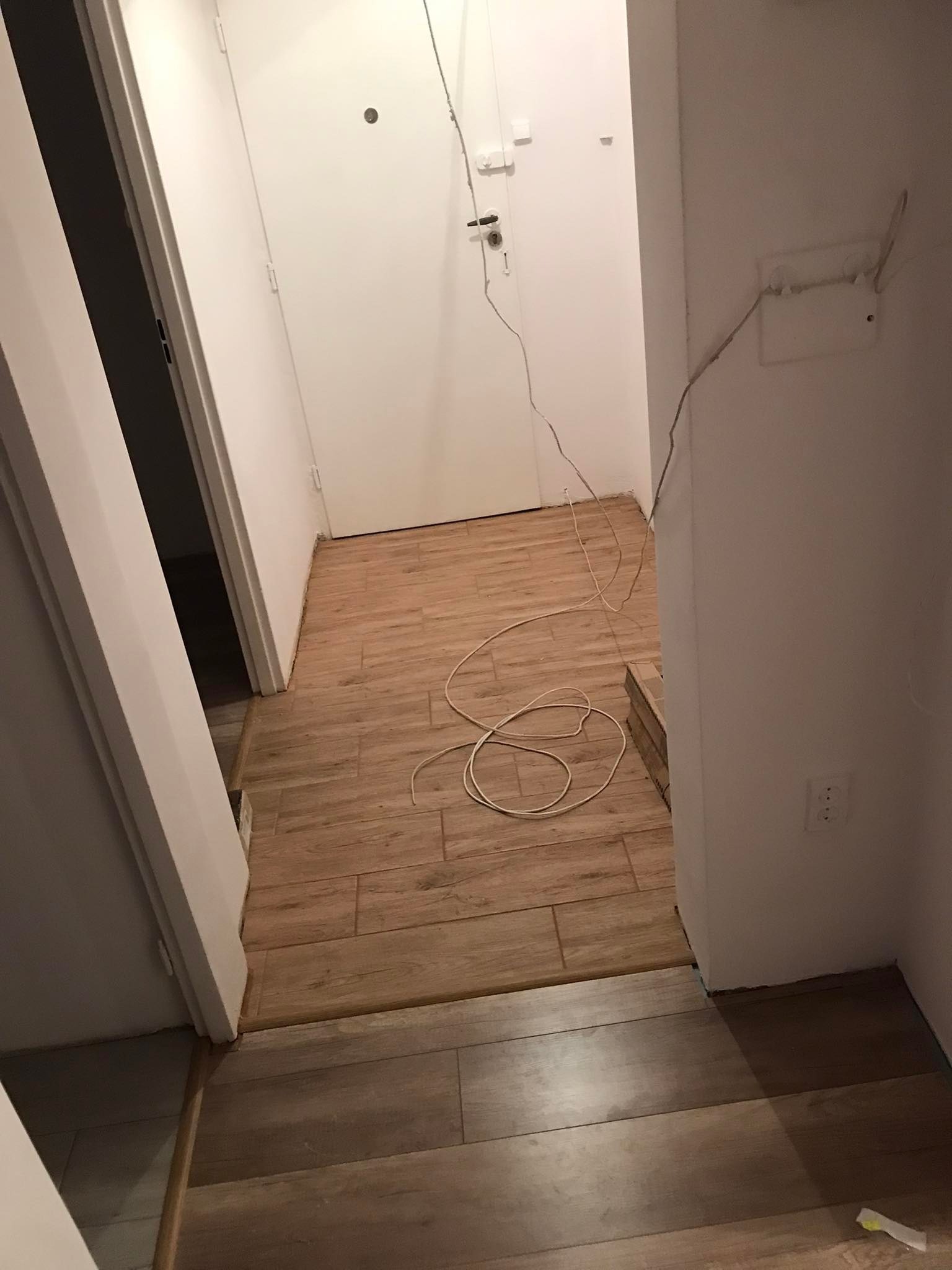 Korytarz w trakcie układania paneli podłogowych z widocznymi kablami wystającymi ze ściany i niezakrytym gniazdkiem elektrycznym.
